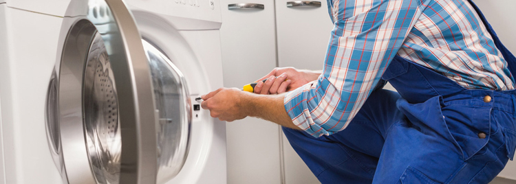 A man in blue overalls fixing a dryer