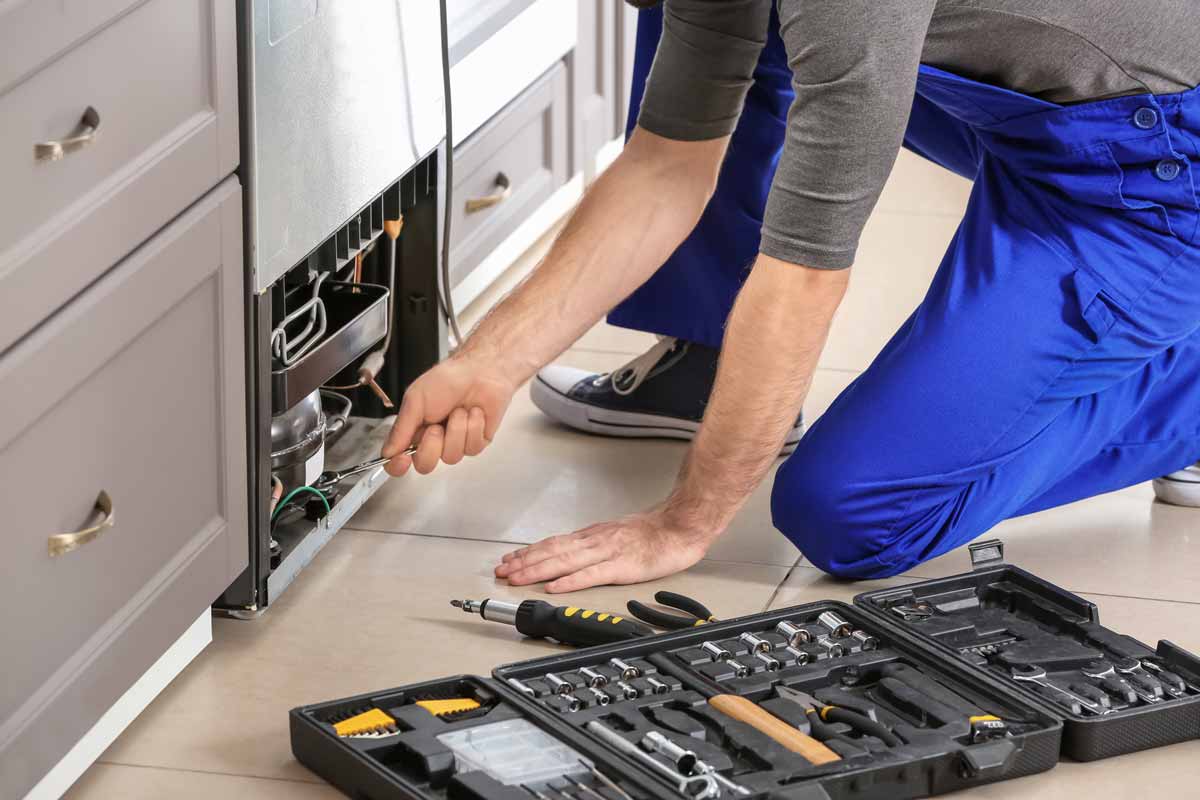 An appliance repair technician kneeling in front of an appliance